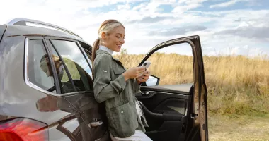 Woman by a car looking at her phone after a vehicle accident on vacation