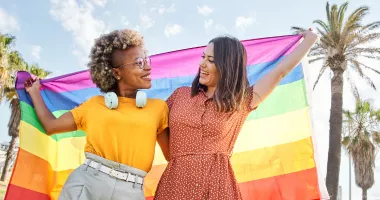 Two smiling women holding a pride flag during their LGTBQ+ travel.