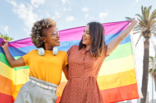 Two smiling women holding a pride flag during their LGTBQ+ travel.