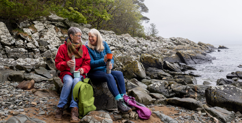 Two women smiling and sitting on rocks in Scotland, which we mention in our U.K. travel guide.