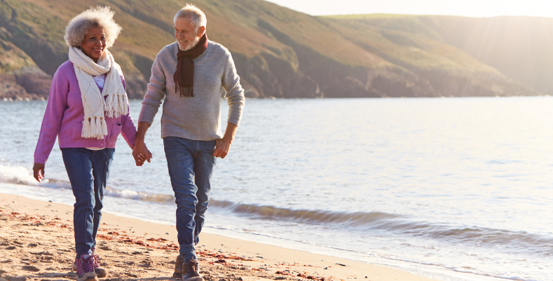 Smiling senior couple walking on the beach in Wales, which we mention in our U.K. travel guide.