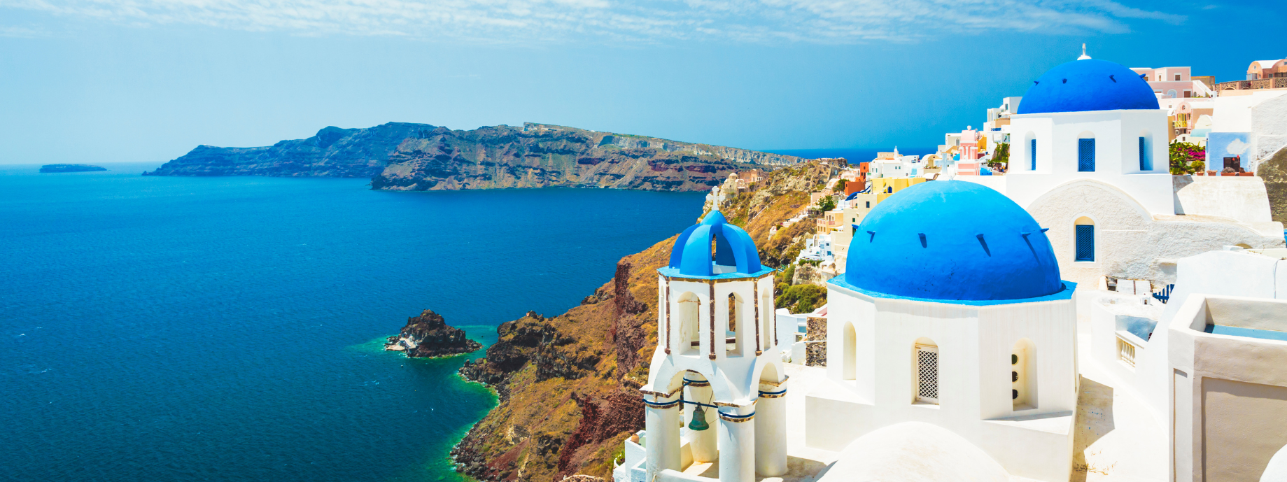 Blue-domed white churches in Oia, Greece, overlooking the ocean where you can travel with travel insurance for Europe