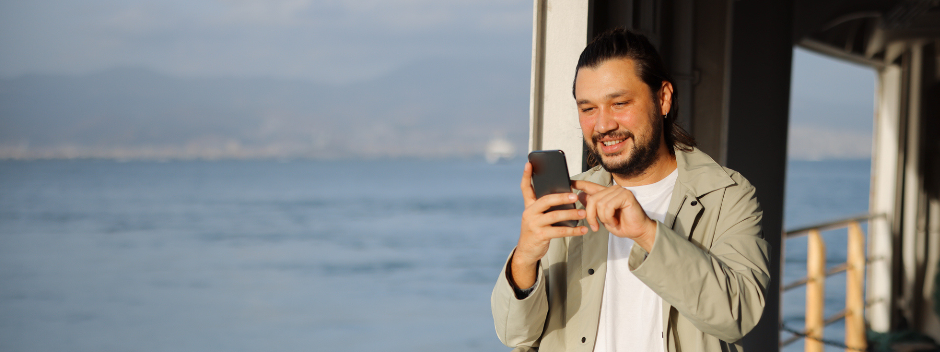 Young smiling man on a ferry looking at his phone for travel assistance