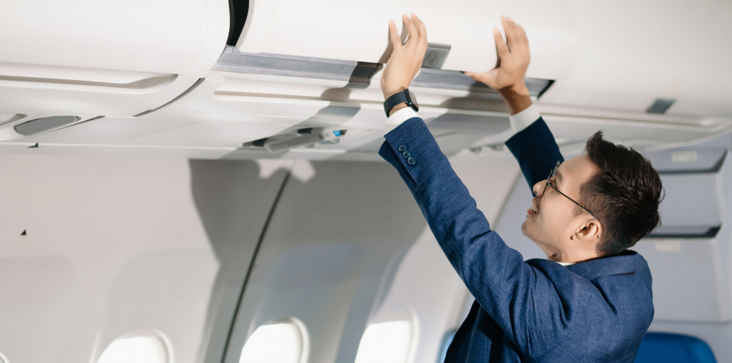 Young man in a suit closing the airplane overhead bin with accidental death travel insurance