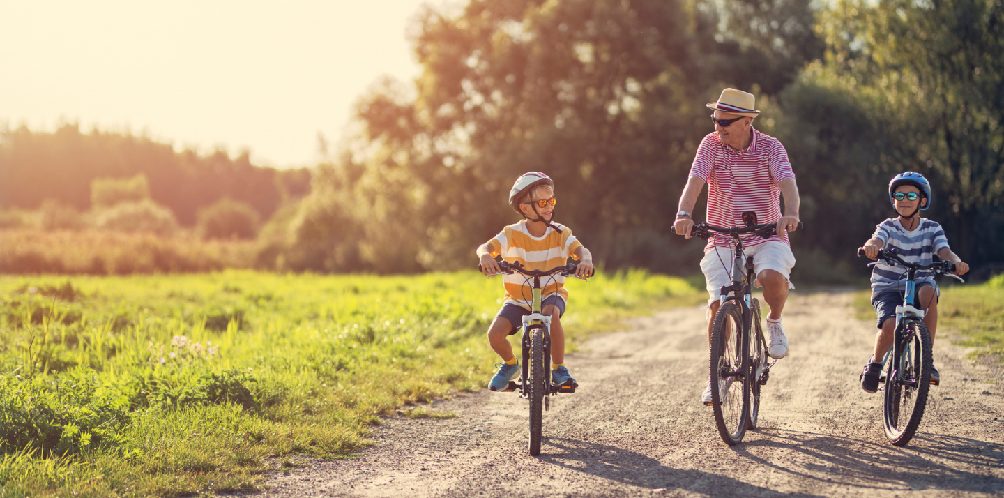 Senior man smiling while biking between his grandsons on vacation with travel insurance with COVID-19 coverage