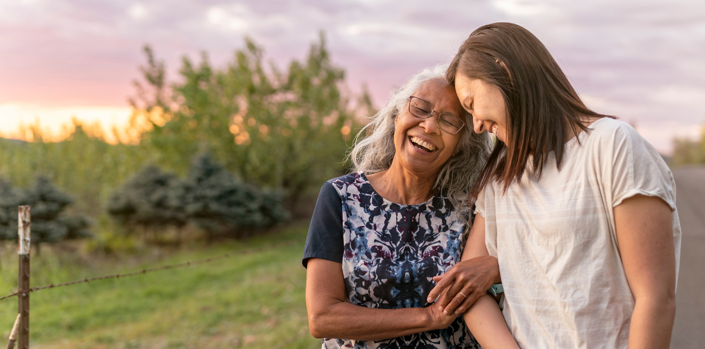 Senior woman with her daughter smiling and linking arms on a walk with travel insurance for pre-existing conditions