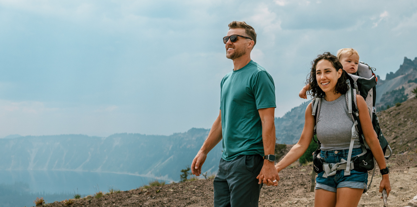 Couple holding hands on a hike with travel insurance with primary coverage while the woman wears their baby in a carrier