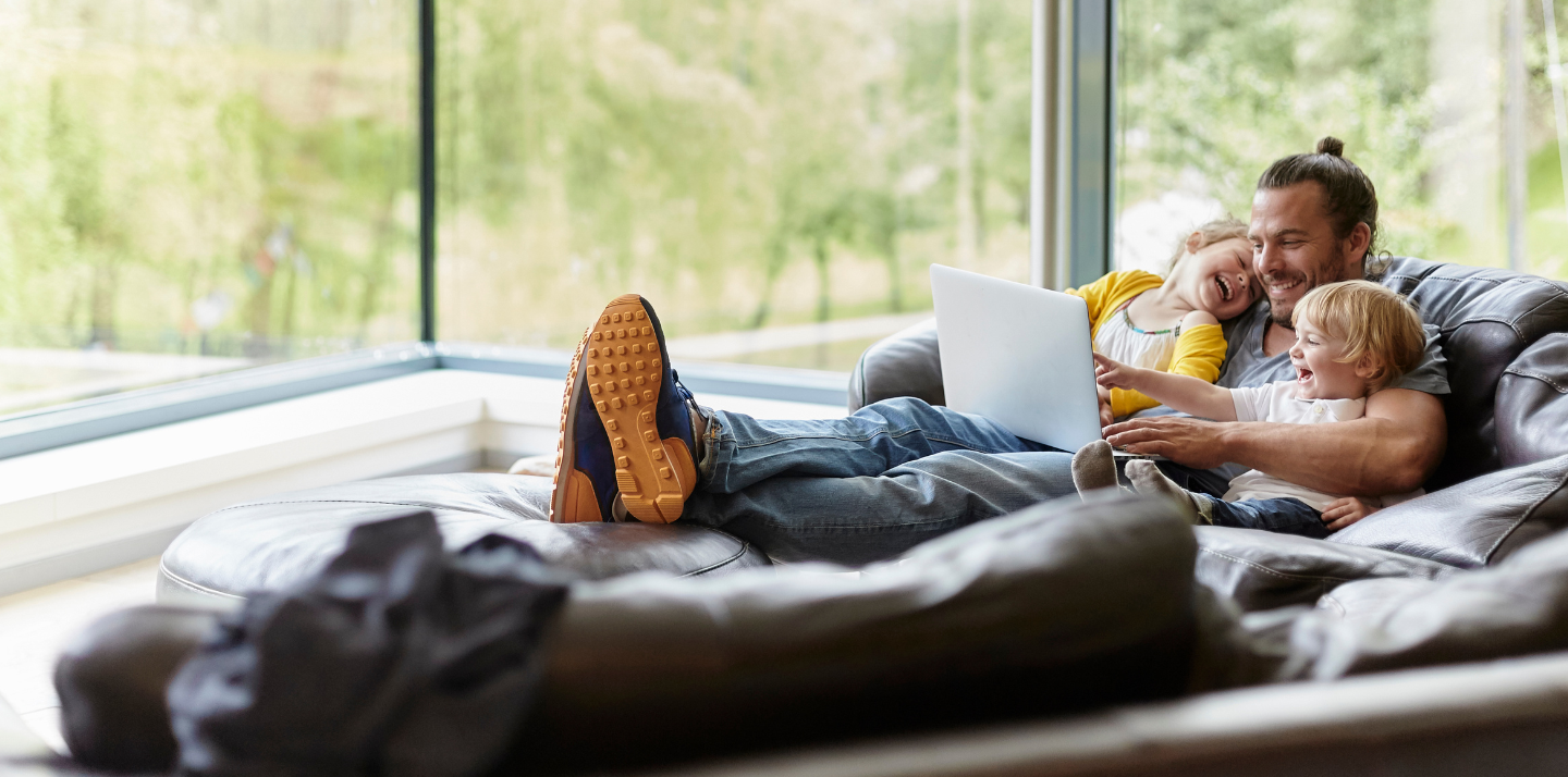 Father smiling with two young children on the couch in front of a laptop with travel insurance for trip cancellation