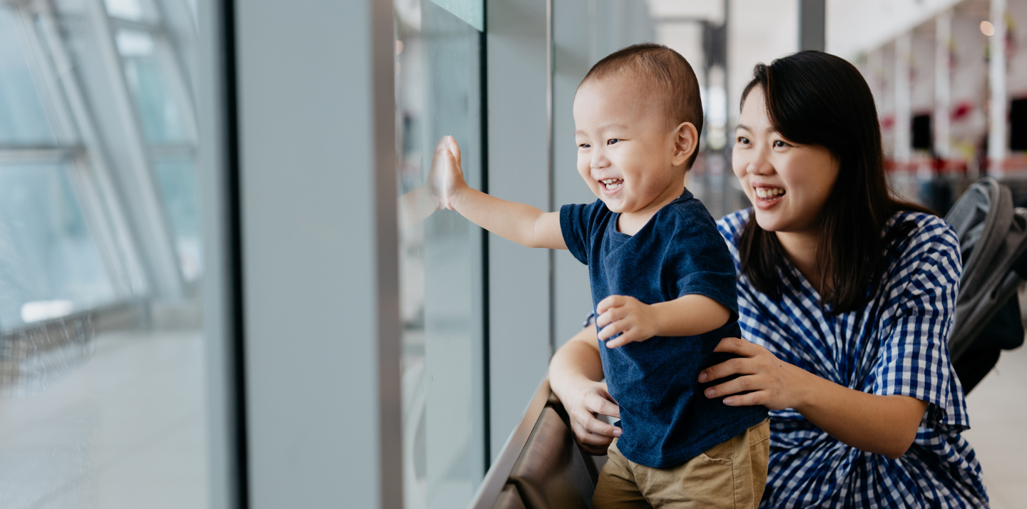 Mother with her young toddler smiling and looking at airplanes with travel delay insurance