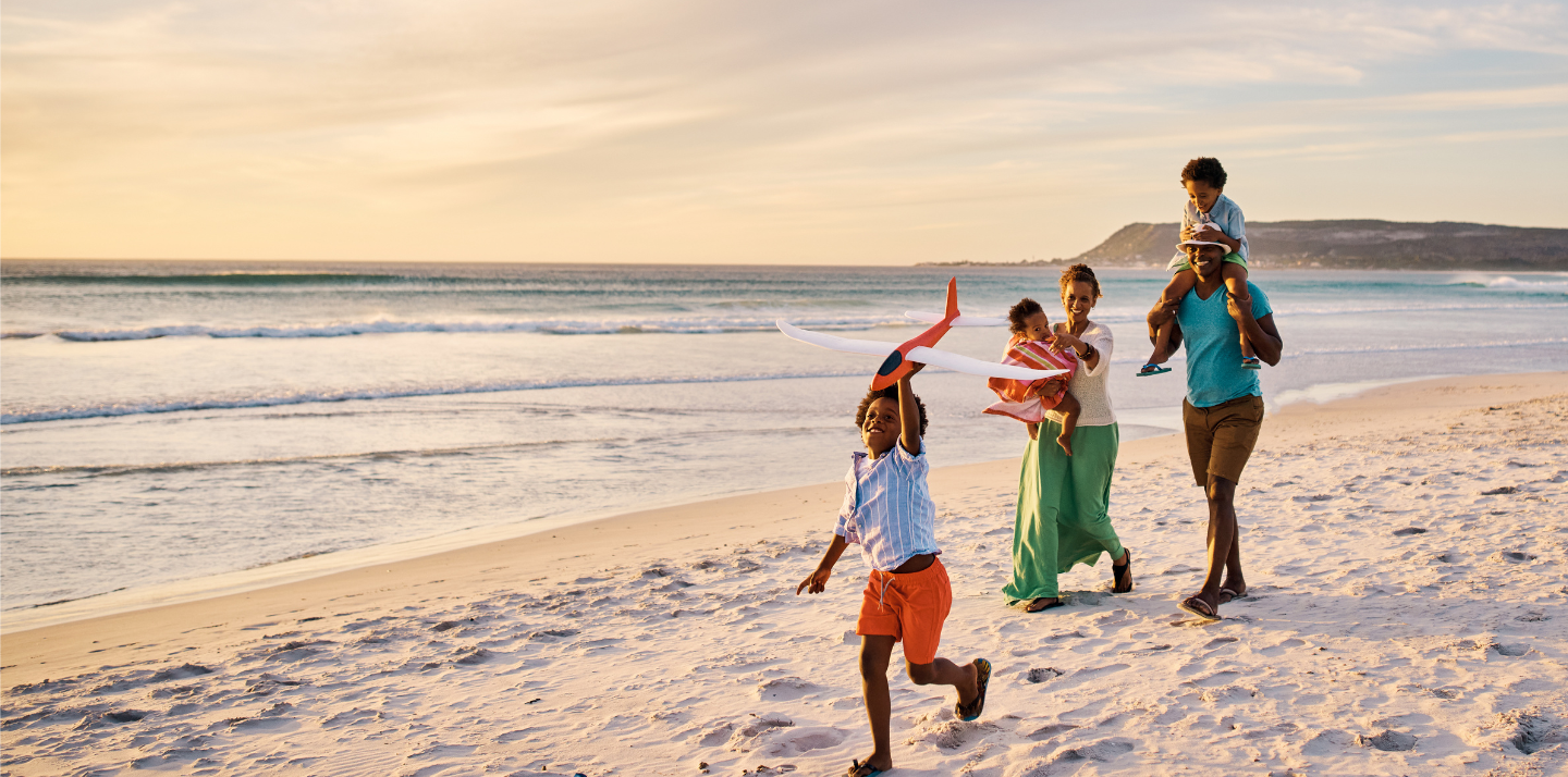 Couple with three young children walking happily on the beach after choosing from travel insurance plans