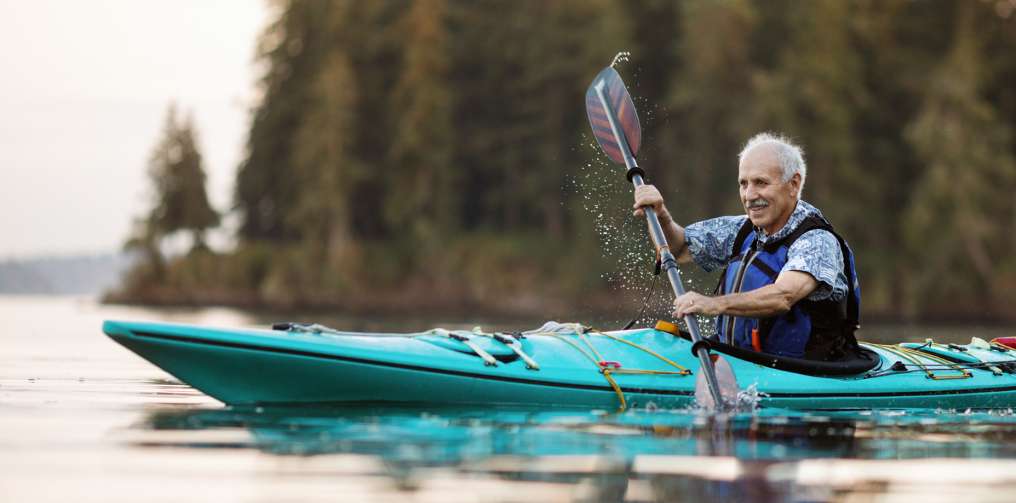 Senior man smiling while kayaking on the Puget Sound in Washington, U.S. with travel insurance upgrades