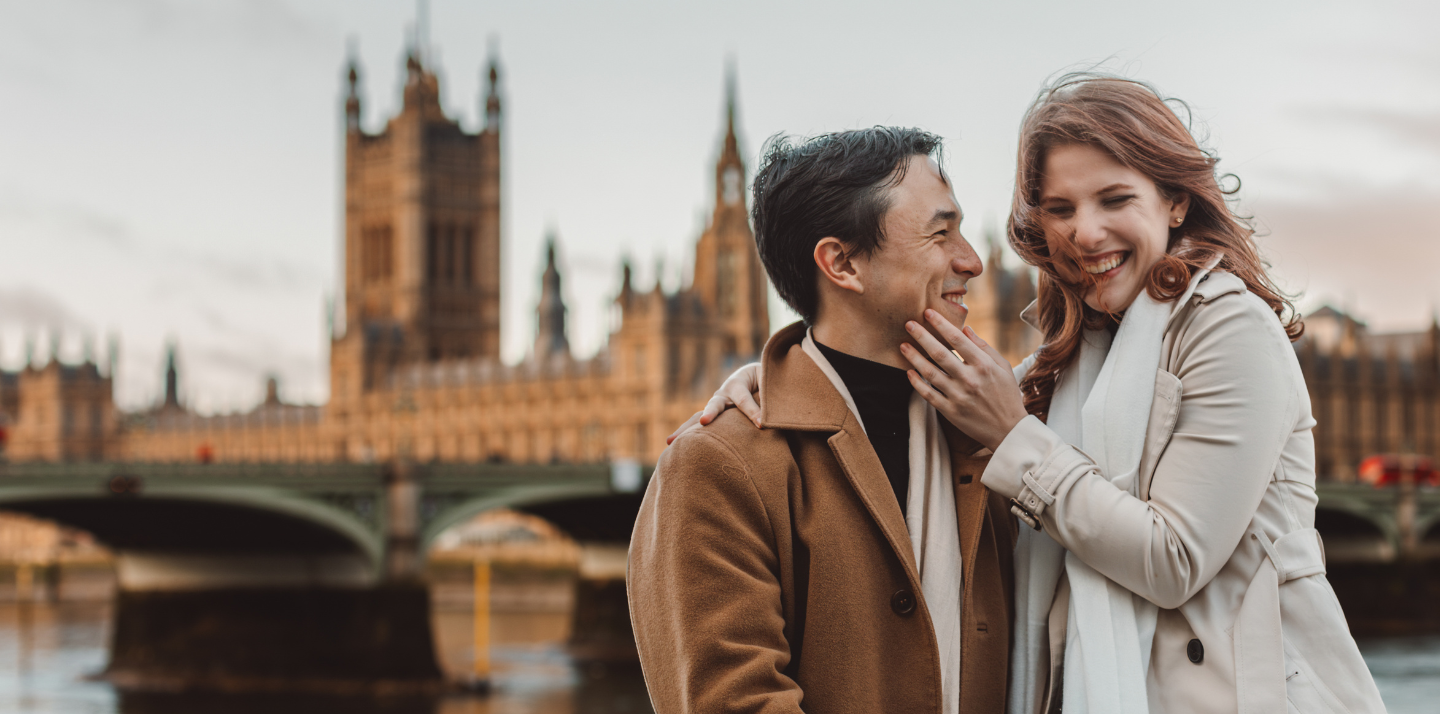 Middle-aged couple smiling and embracing in London with Westminster Bridge in the background after choosing from types of travel insurance