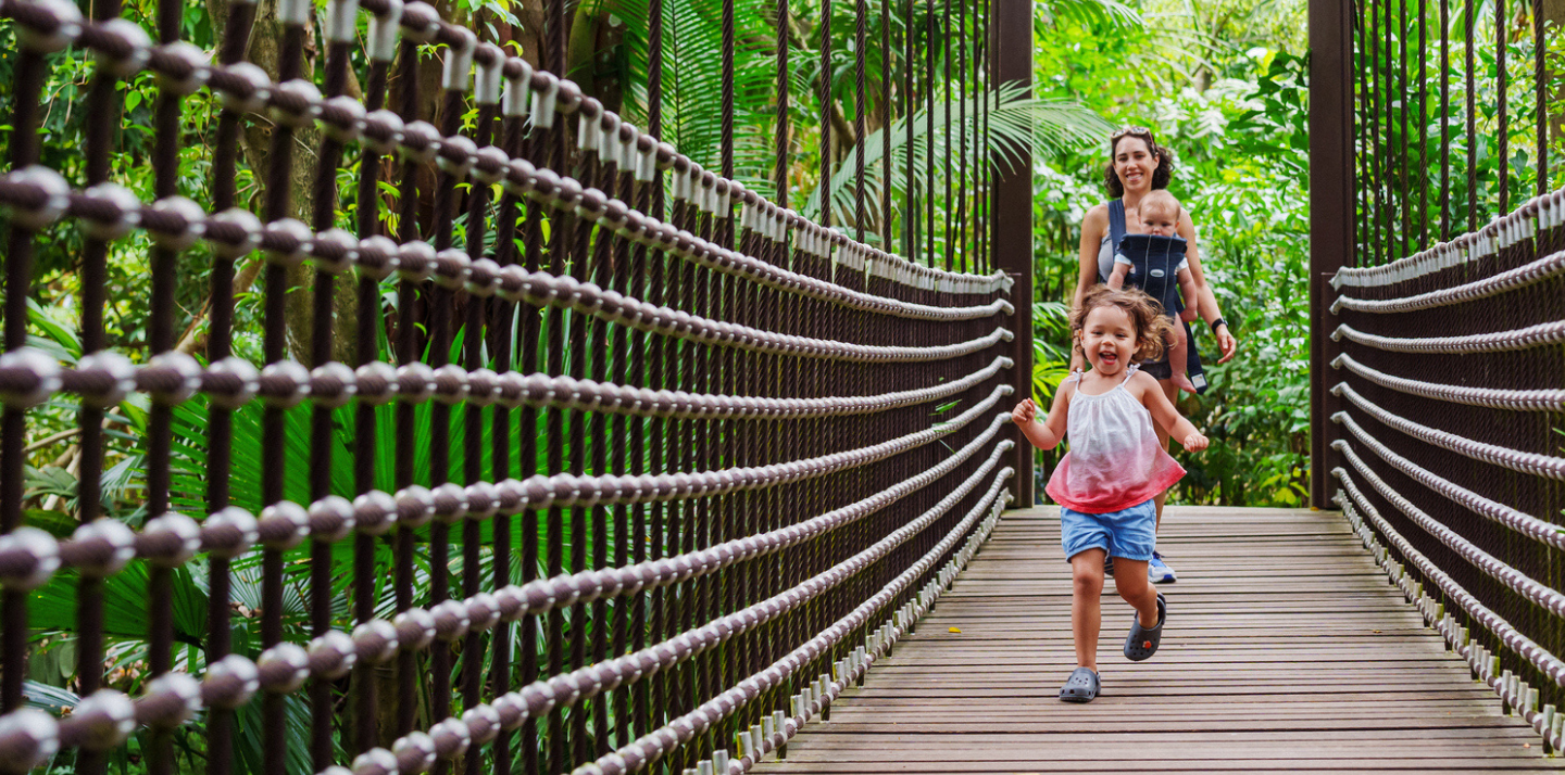 Happy girl running on a Singapore bridge and smiling woman with international travel insurance and baby in background