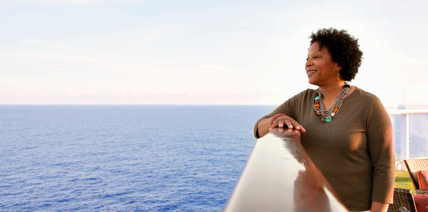 Middle-aged woman with cruise travel insurance smiling and looking at the ocean with her hand on the railing