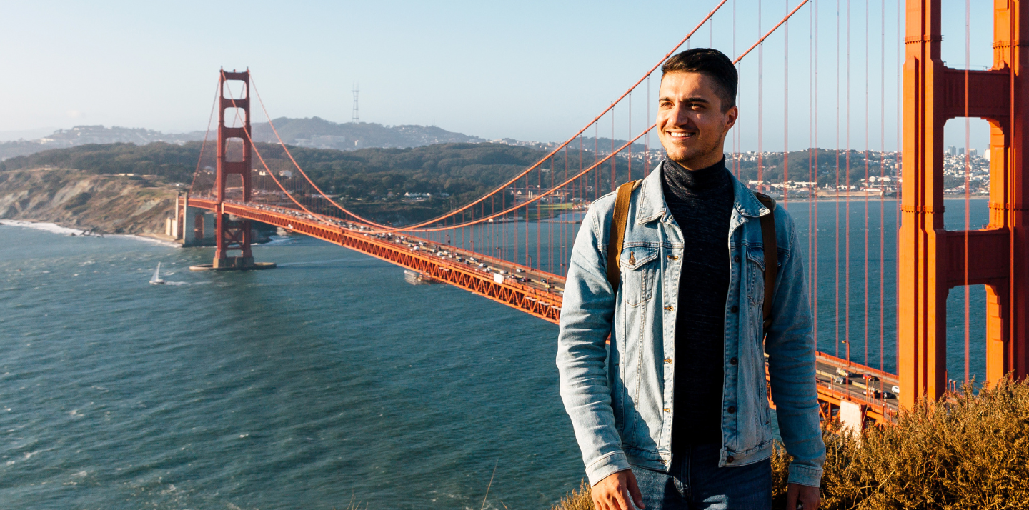 Young man with domestic travel insurance smiling with the Golden Gate Bridge in the background in San Francisco