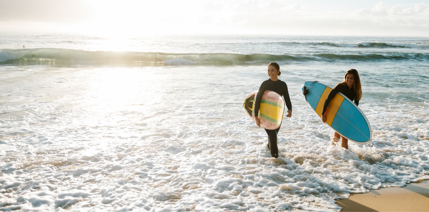 Two young women holding their surfboards walking out of the ocean in Australia