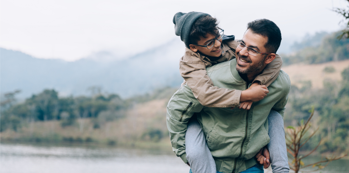 father giving his son a piggy-back ride and smiling while traveling with comprehensive travel insurance