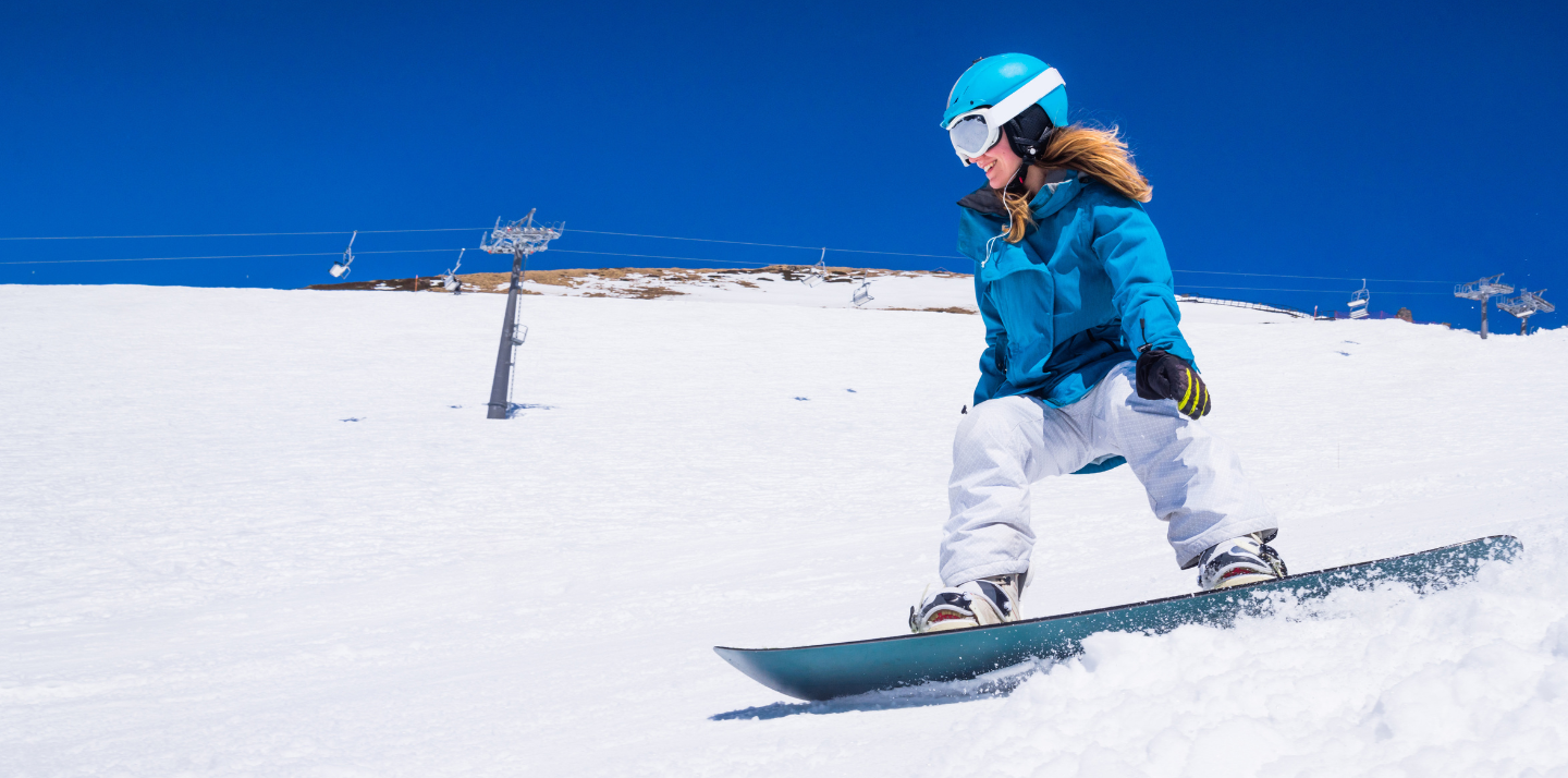 Woman snowboarding down a hill with snowboarding and skiing travel insurance