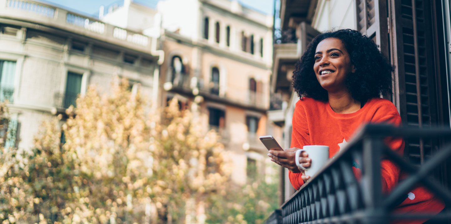 Woman standing on a balcony with coffee in Barcelona using her phone to learn more about Travelex