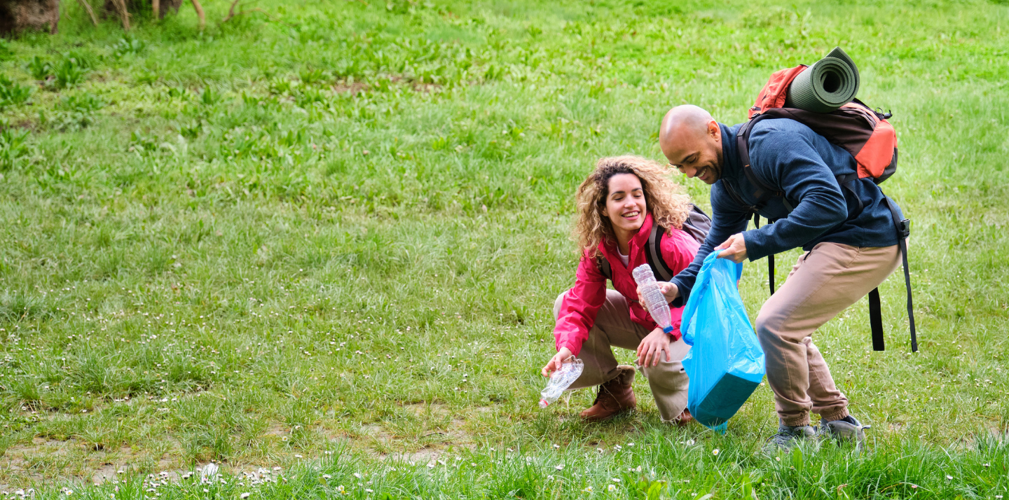 Man and woman smiling with camping backpacks on while picking up trash with volunteer travel insurance