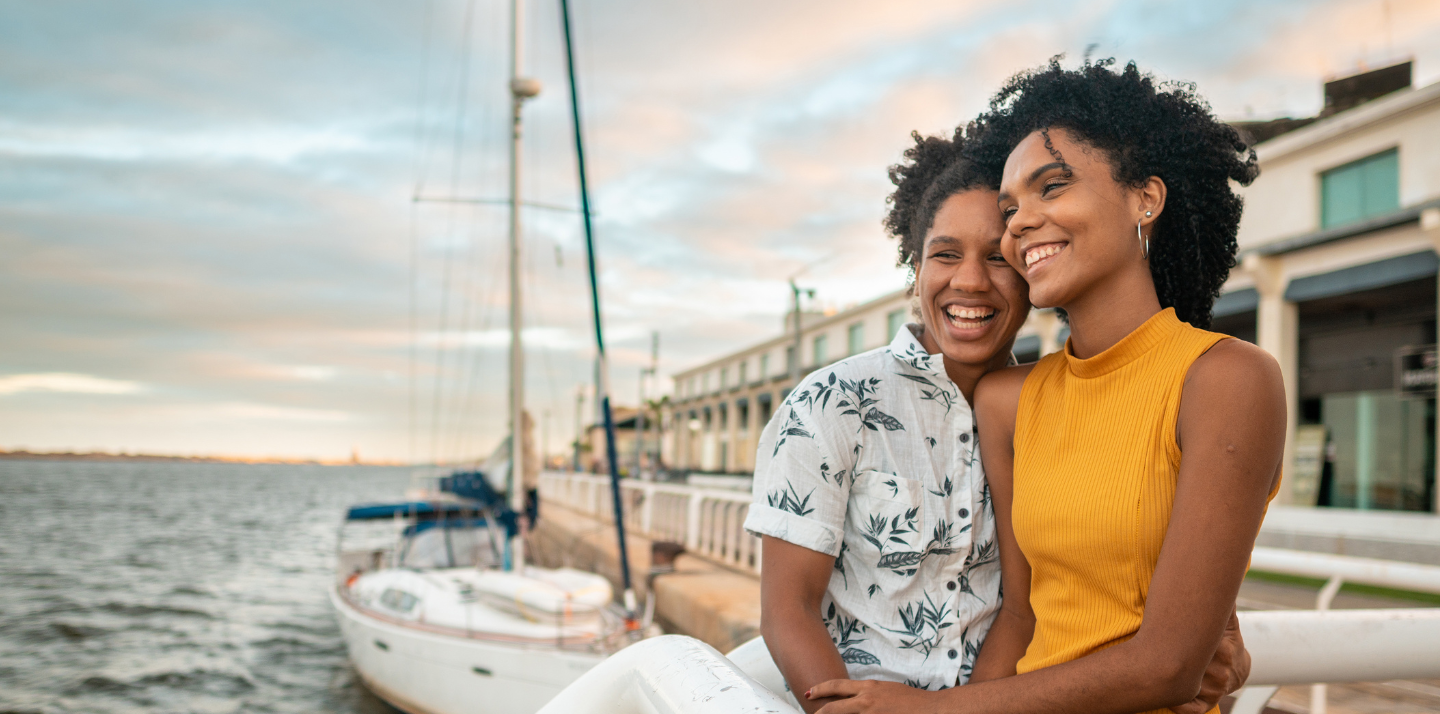 Two young women holding each other and looking at the ocean with a boat in the background in Marco Zero in Brazil