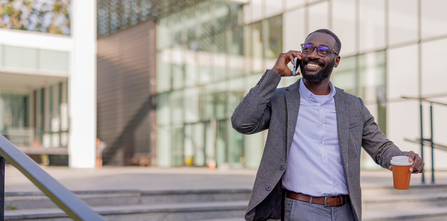 Man on the phone holding coffee and smiling in front of an office building with business travel insurance