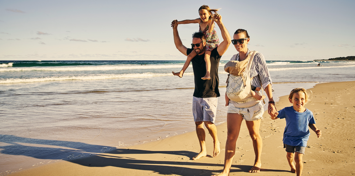 Man and woman with three young children walking together on the beach with family travel insurance