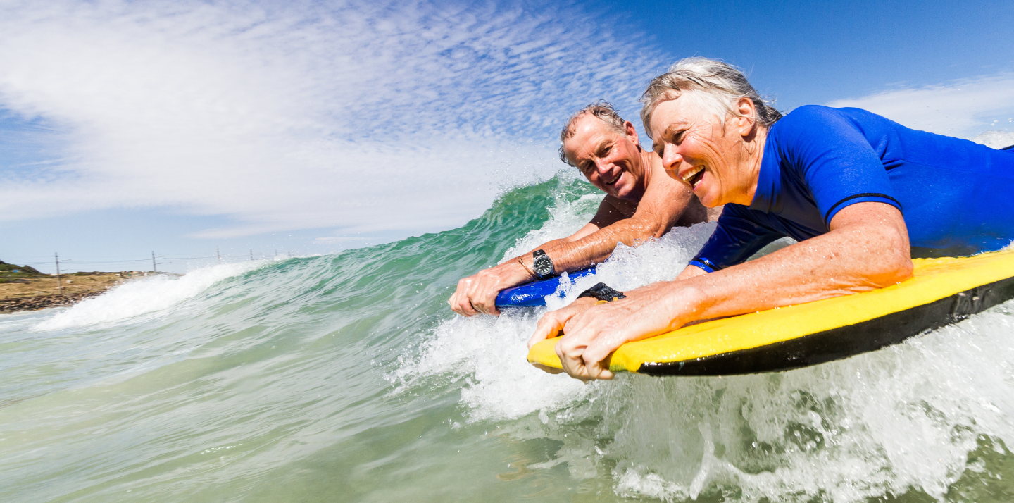 Senior man and woman boogie boarding on a wave in the ocean with senior travel insurance in Cape Town, South Africa