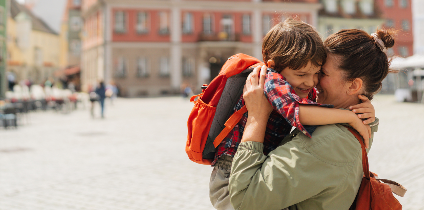 Woman smiling and hugging her young son wearing a backpack in Germany after reading Travelex insurance reviews