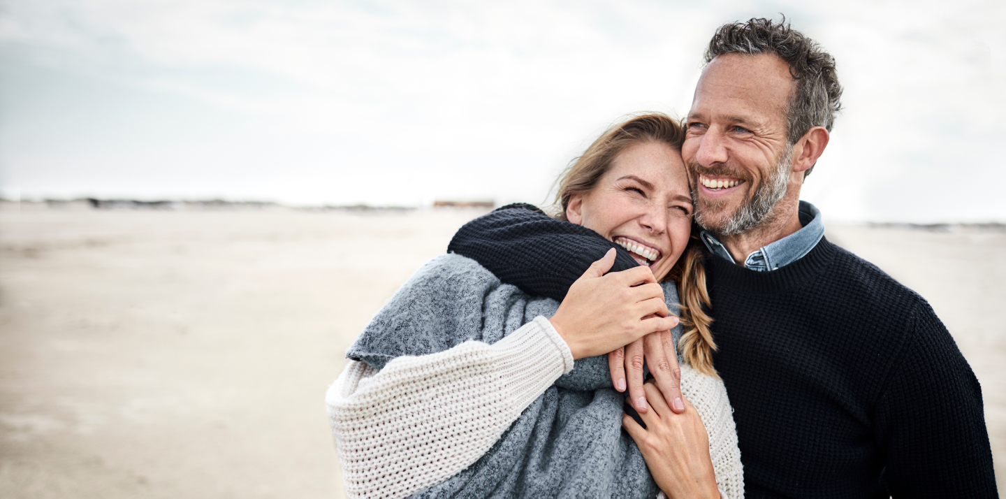 Middle-aged man with his arm around a middle-aged woman smiling on the beach