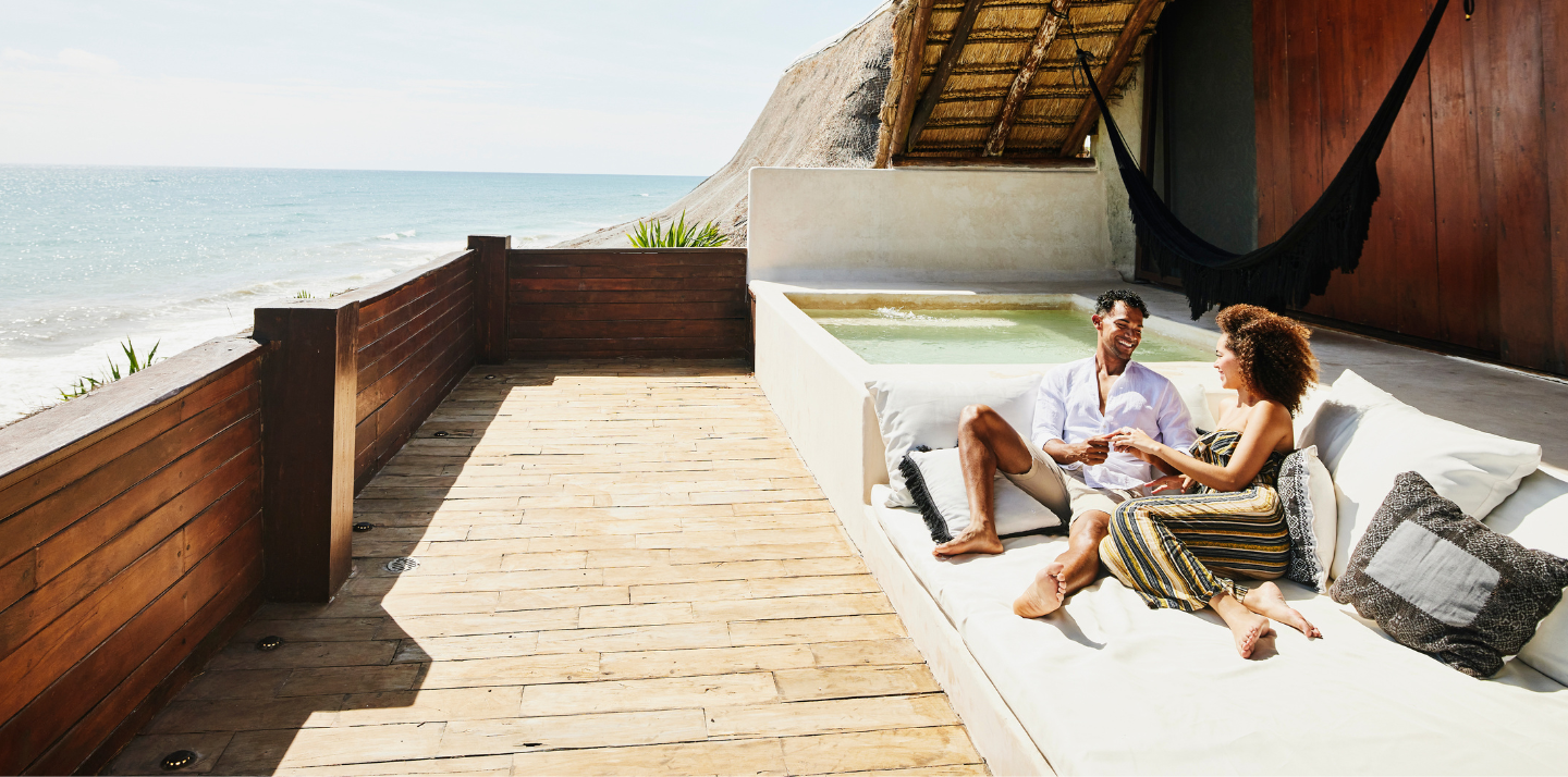 Smiling couple on an outdoor sofa at their accommodation overlooking the ocean in Quintana Roo, Mexico