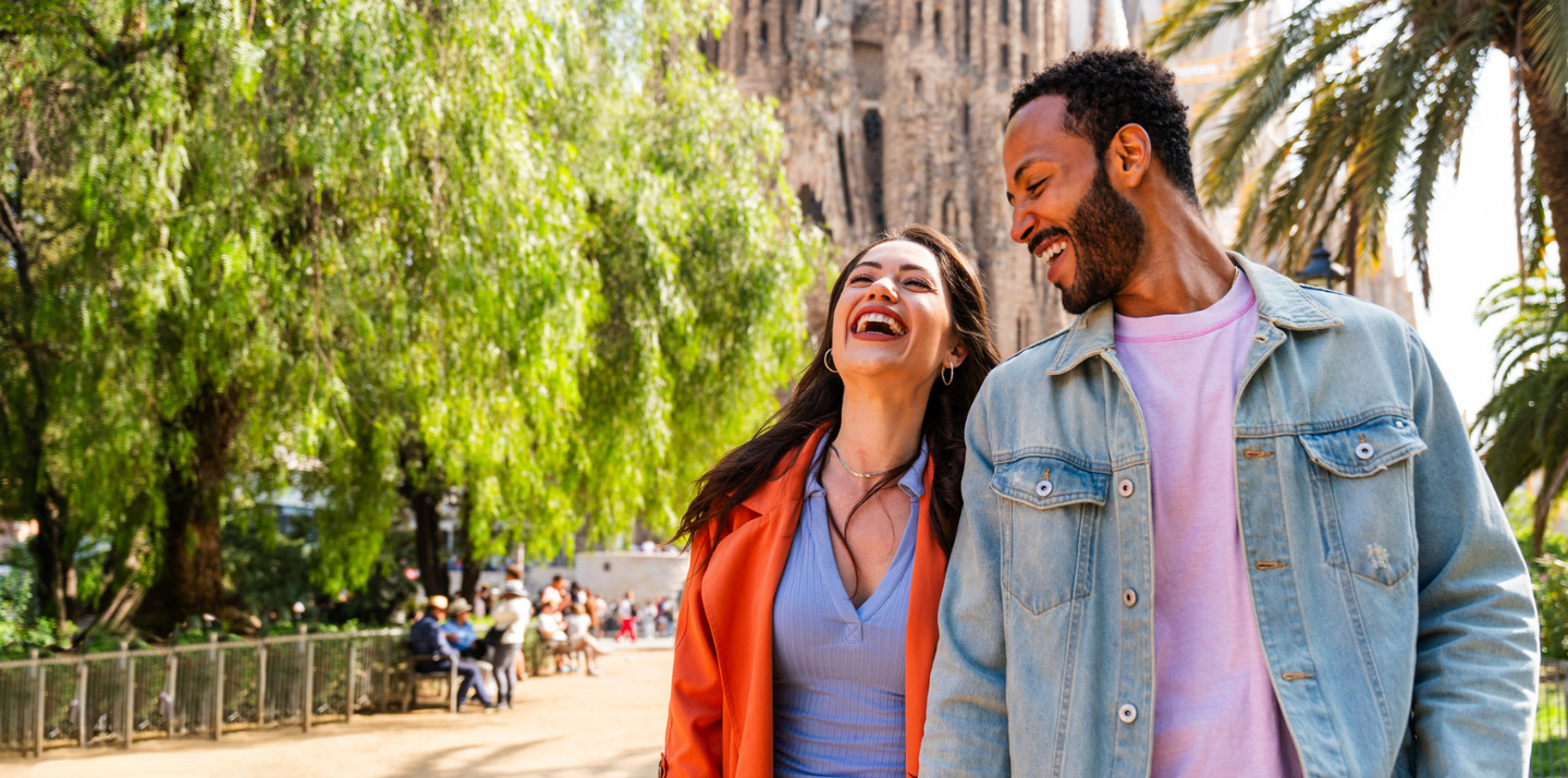 Multiracial smiling couple in front of Sagrada Familia in Barcelona traveling with cheap travel insurance