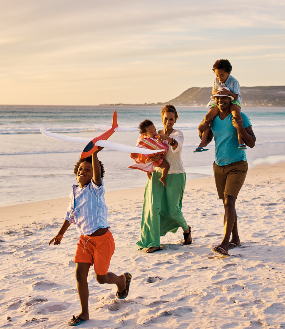 Couple with three young children walking happily on the beach after choosing from travel insurance plans