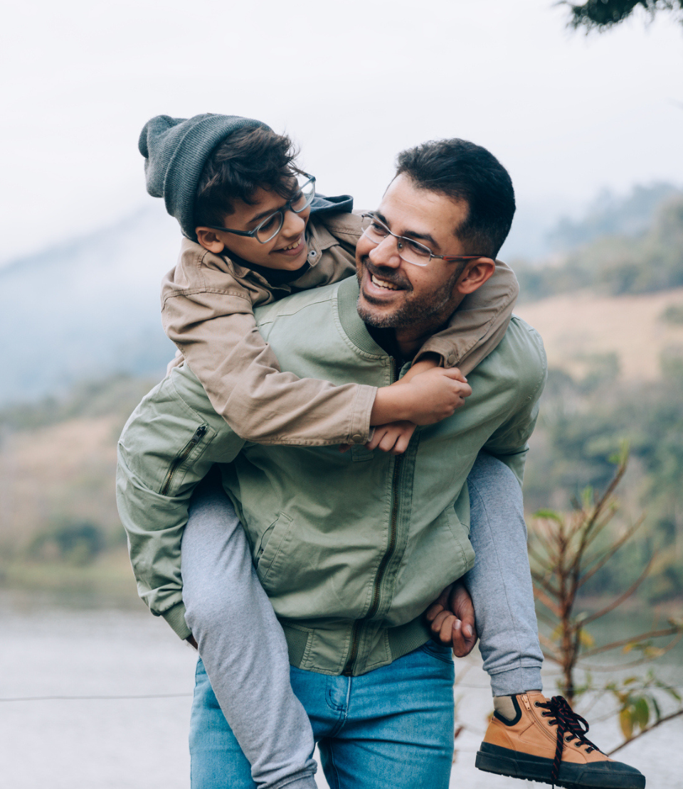 father giving his son a piggy-back ride and smiling while traveling with comprehensive travel insurance