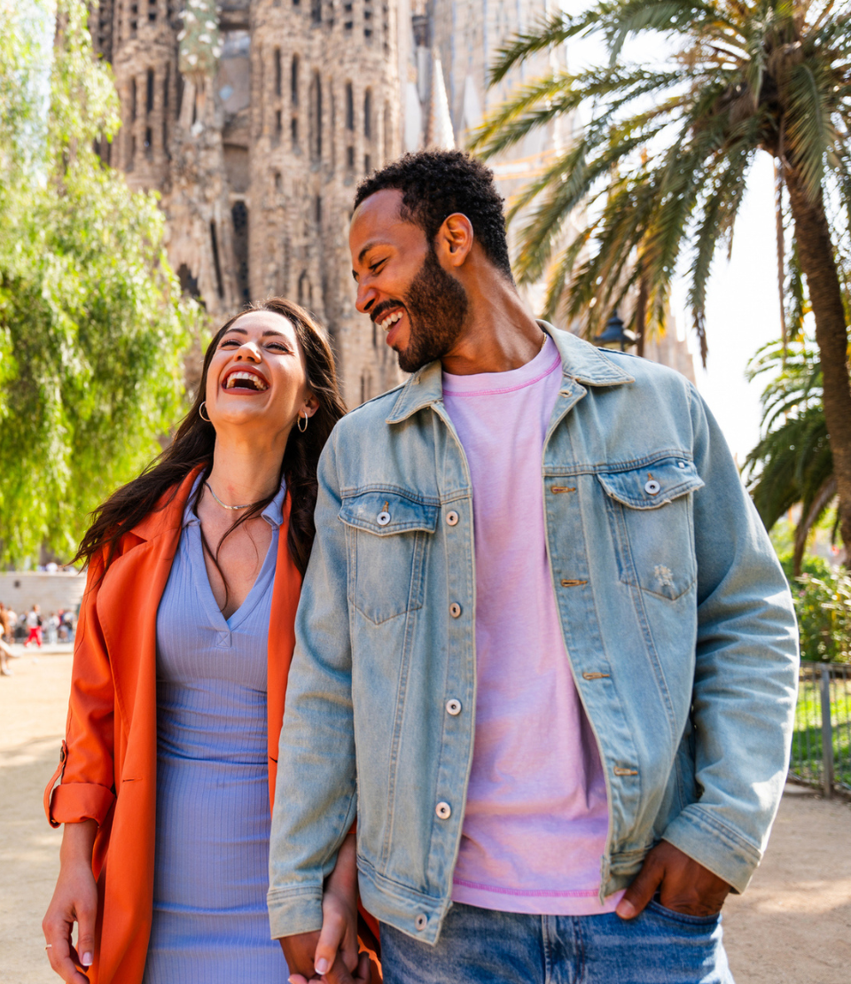 Multiracial smiling couple in front of Sagrada Familia in Barcelona traveling with cheap travel insurance