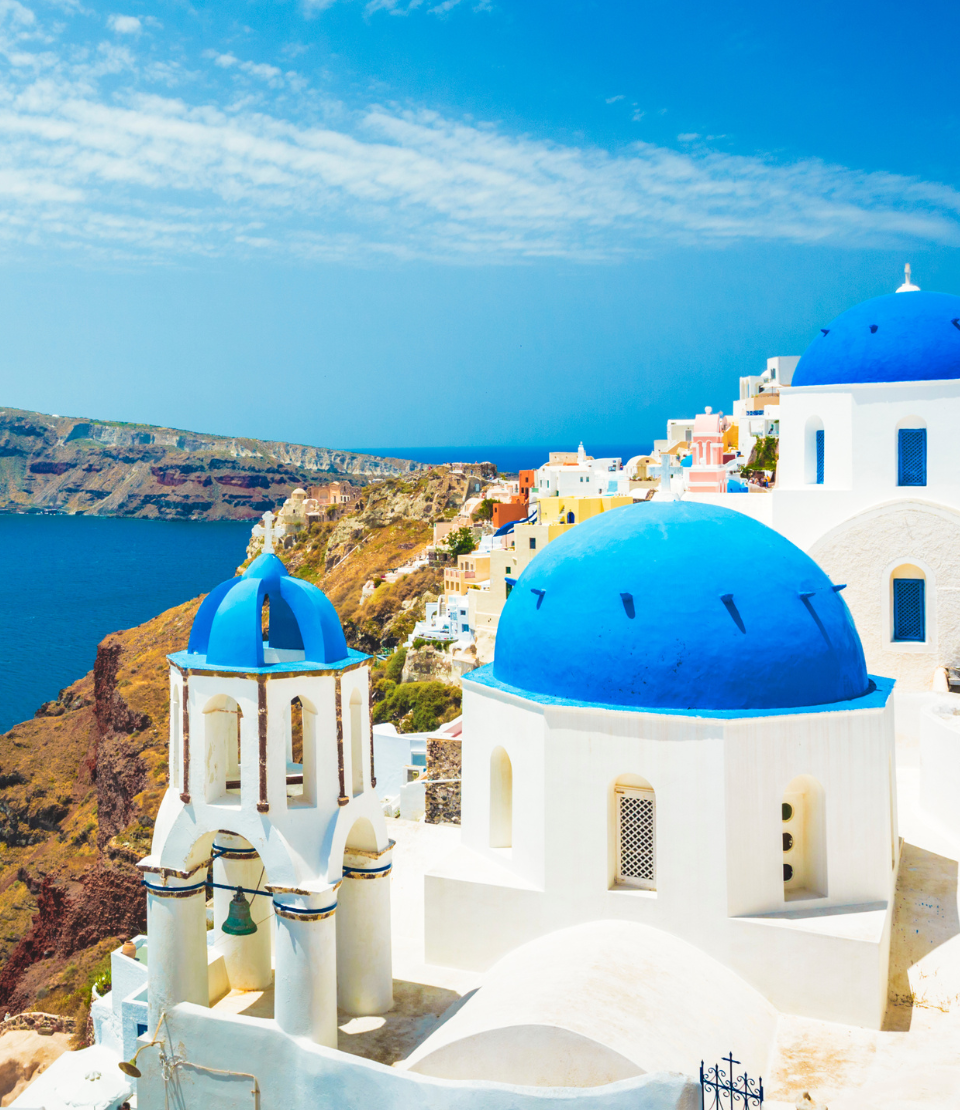 Blue-domed white churches in Oia, Greece, overlooking the ocean where you can travel with travel insurance for Europe