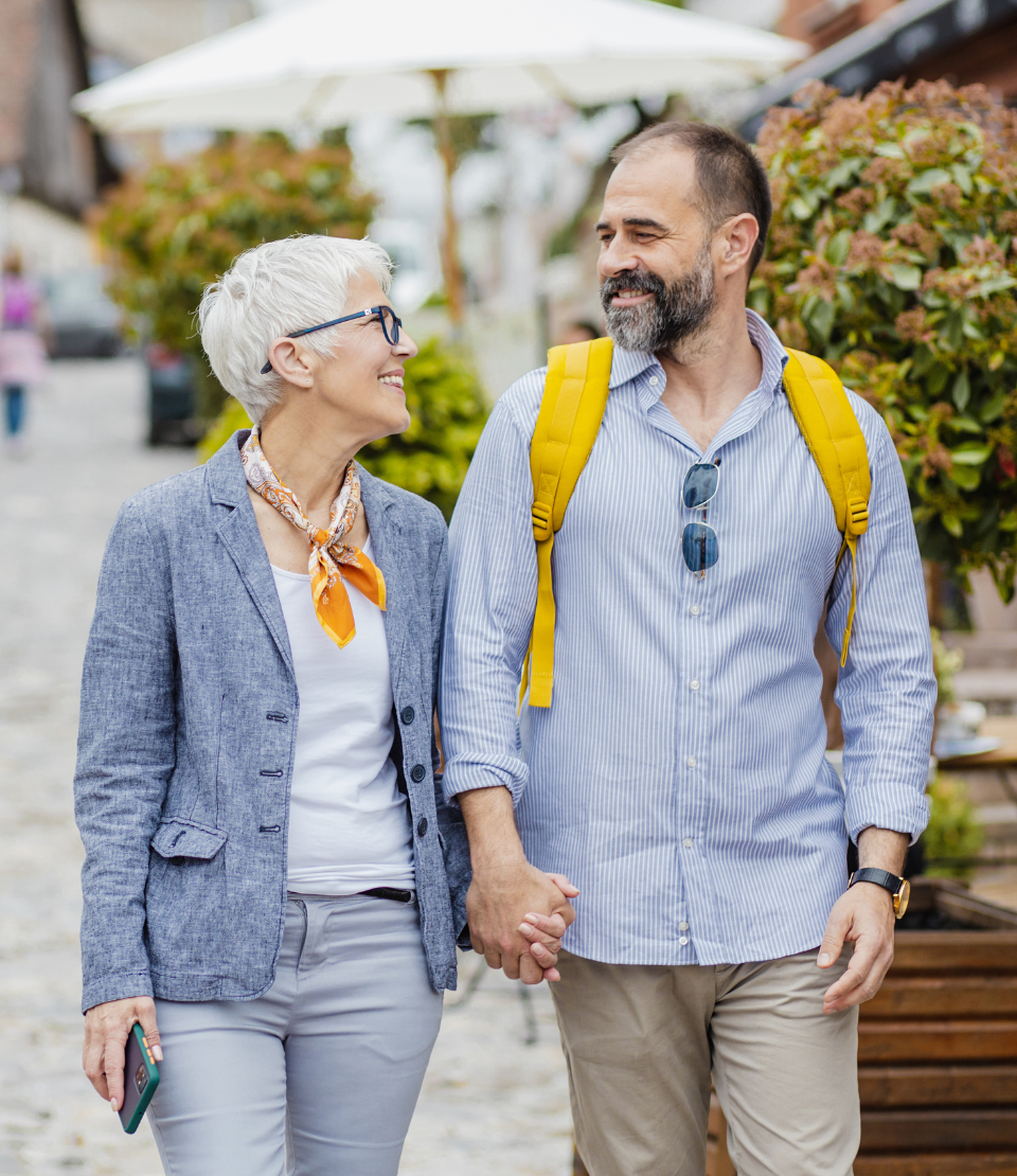 Senior couple smiling and holding hands on the street while traveling with cheap travel insurance