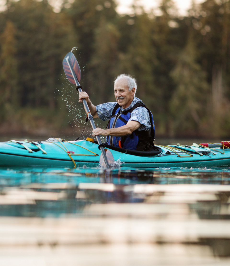 Senior man smiling while kayaking on the Puget Sound in Washington, U.S. with travel insurance upgrades