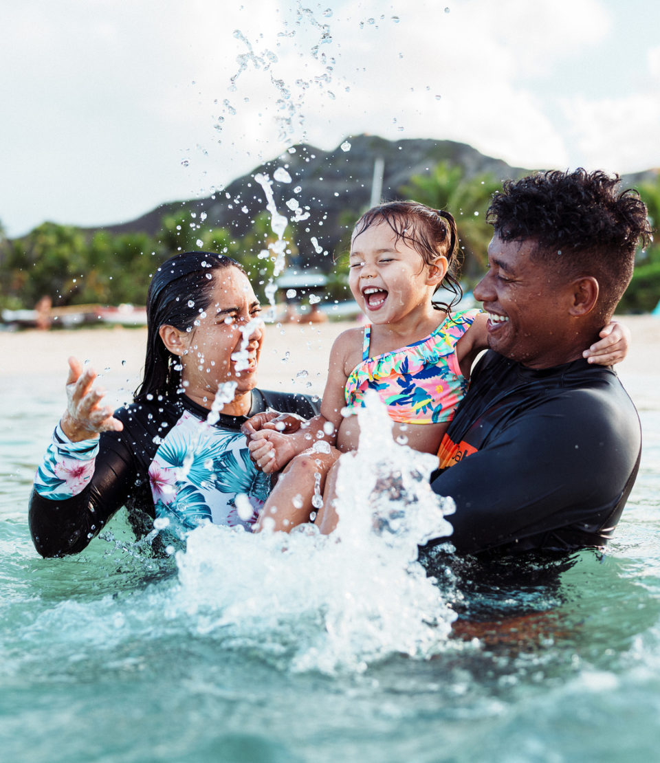 Multiracial couple with young daughter splashing in the ocean and smiling while traveling with travel insurance benefits