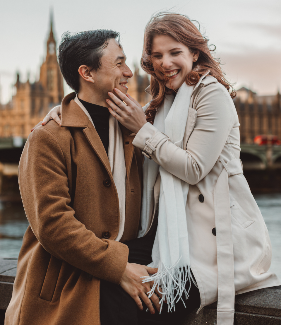 Middle-aged couple smiling and embracing in London with Westminster Bridge in the background after choosing from types of travel insurance