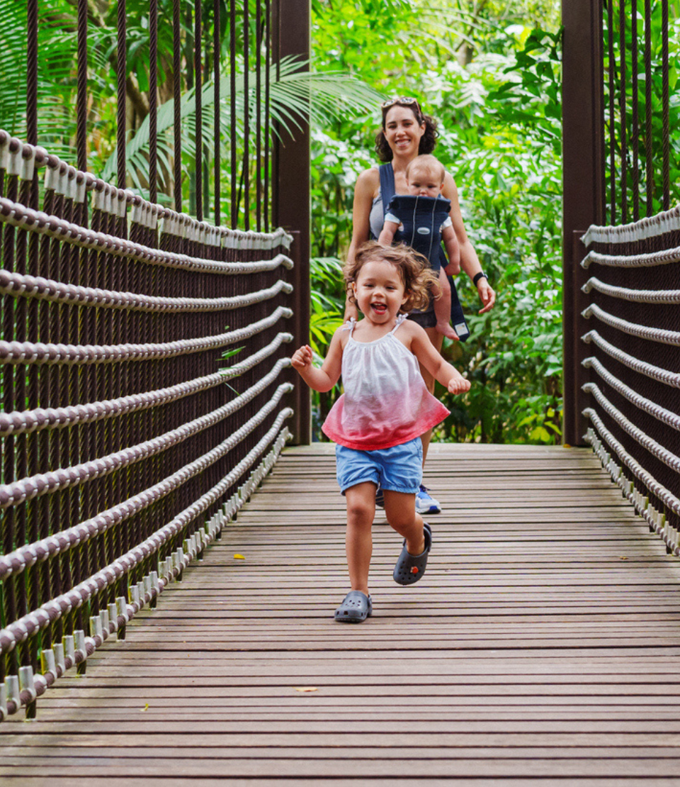 Happy girl running on a Singapore bridge and smiling woman with international travel insurance and baby in background