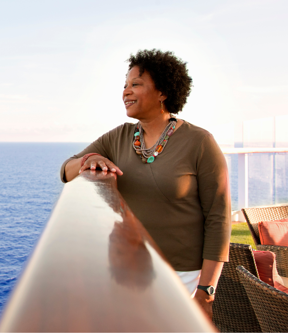 Middle-aged woman with cruise travel insurance smiling and looking at the ocean with her hand on the railing