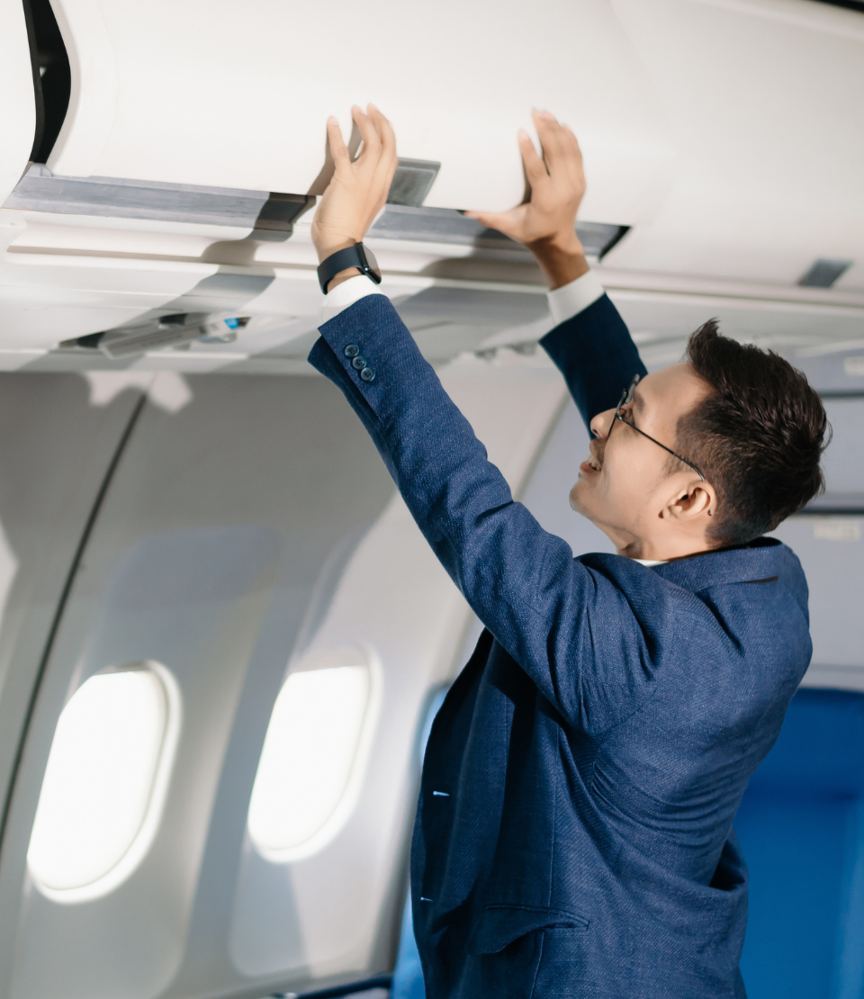 Young man in a suit closing the airplane overhead bin with accidental death travel insurance