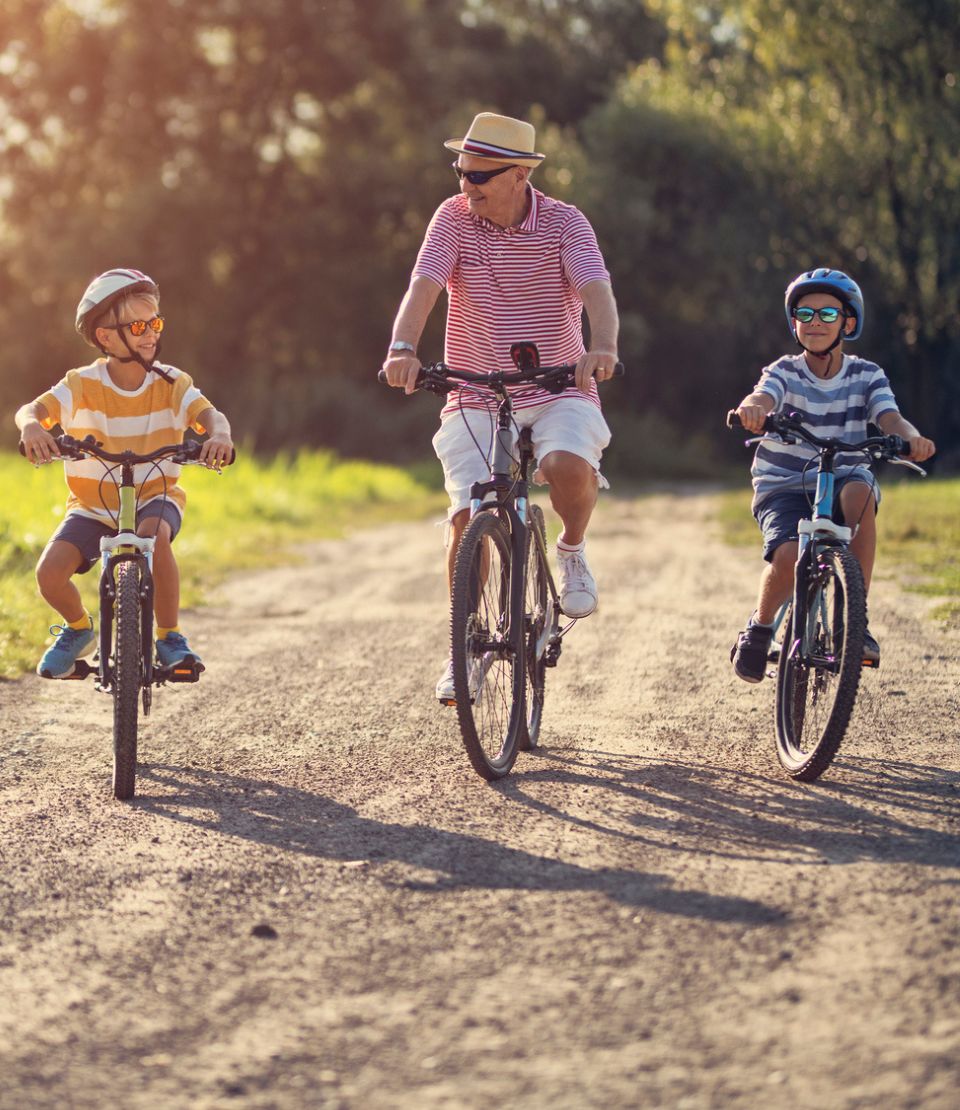 Senior man smiling while biking between his grandsons on vacation with travel insurance with COVID-19 coverage