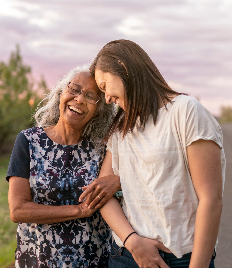 Senior woman with her daughter smiling and linking arms on a walk with travel insurance for pre-existing conditions