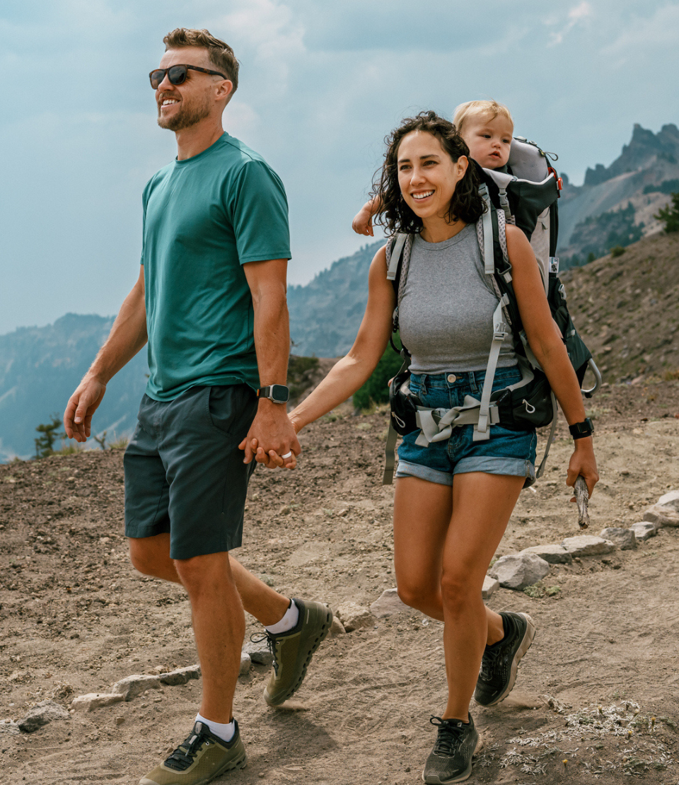 Couple holding hands on a hike with travel insurance with primary coverage while the woman wears their baby in a carrier