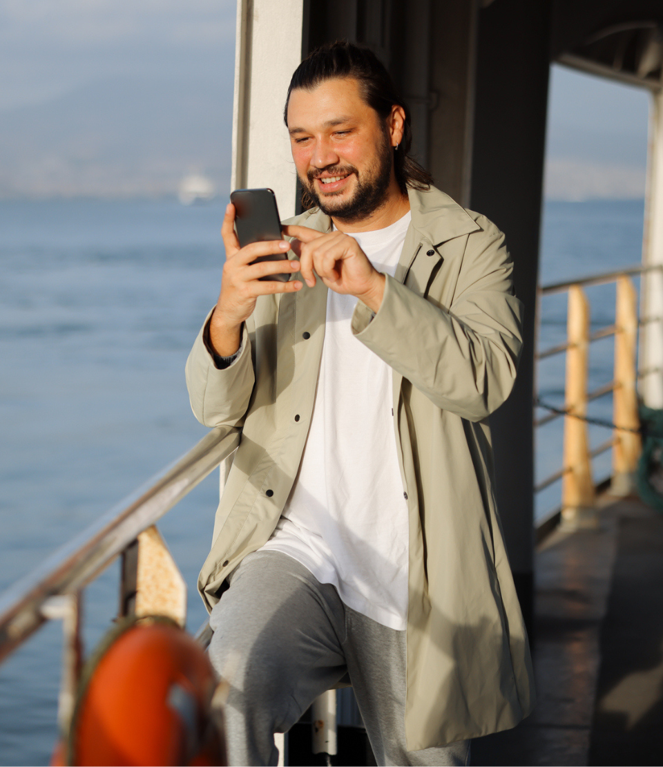 Young smiling man on a ferry looking at his phone for travel assistance