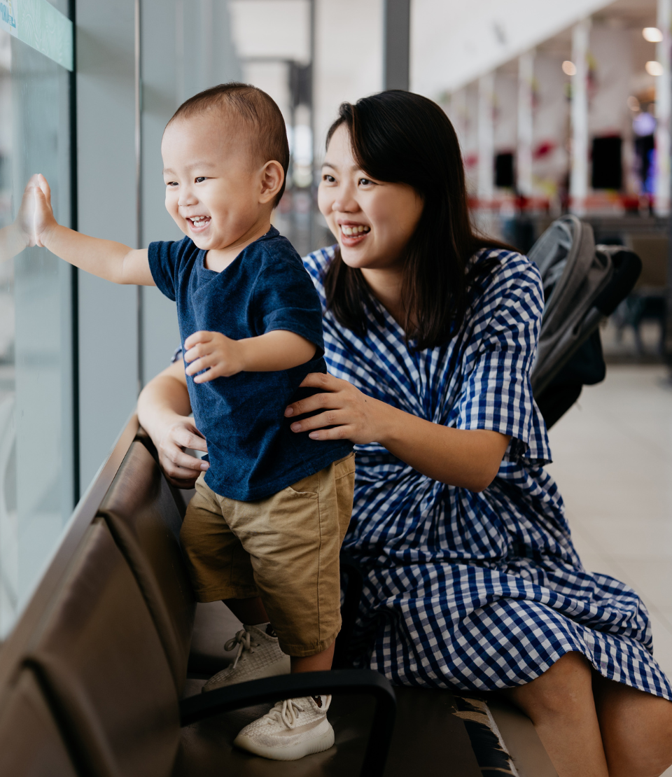 Mother with her young toddler smiling and looking at airplanes with travel delay insurance