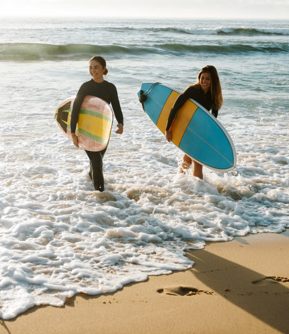 Two young women holding their surfboards walking out of the ocean in Australia