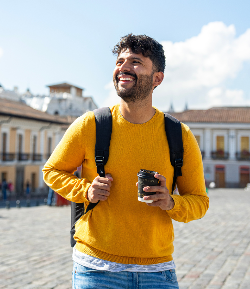 Young man smiling with a backpack and holding coffee in front of San Francisco church in Quito, Ecuador